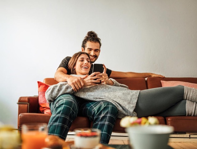 Paar liegt auf der Couch und schaut auf ein Smartphone.
