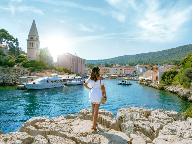 StÃ¶bere durch unsere Flugangebote fÃ¼r 2025. Junge Frau blickt auf den Hafen von Veli Losinj in Kroatien.