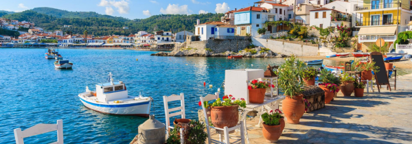 Blick auf eine Bucht in Griechenland mit HÃ¤usern, Pflanzen und Booten auf dem Wasser.