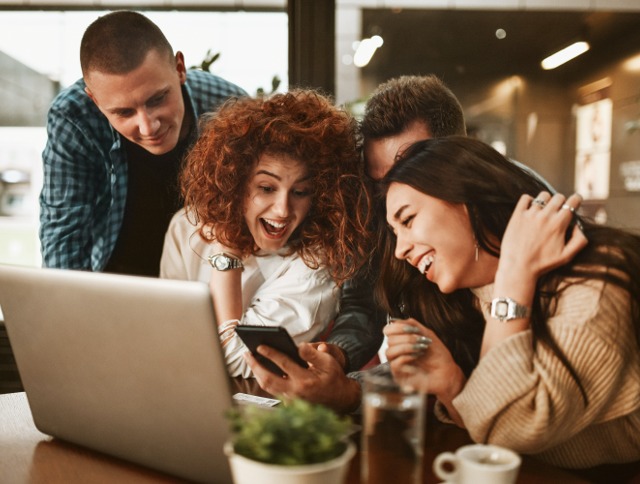 Vier Freund:innen sitzen vor dem Laptop und buchen per Blind Booking, jetzt ausprobieren!